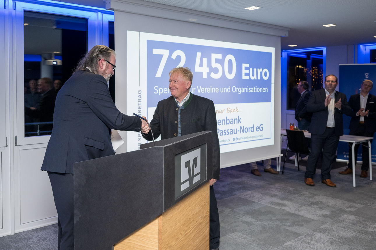 Ein Mann mit einem Mikrofon wärend er einem Mann die Hand reicht.