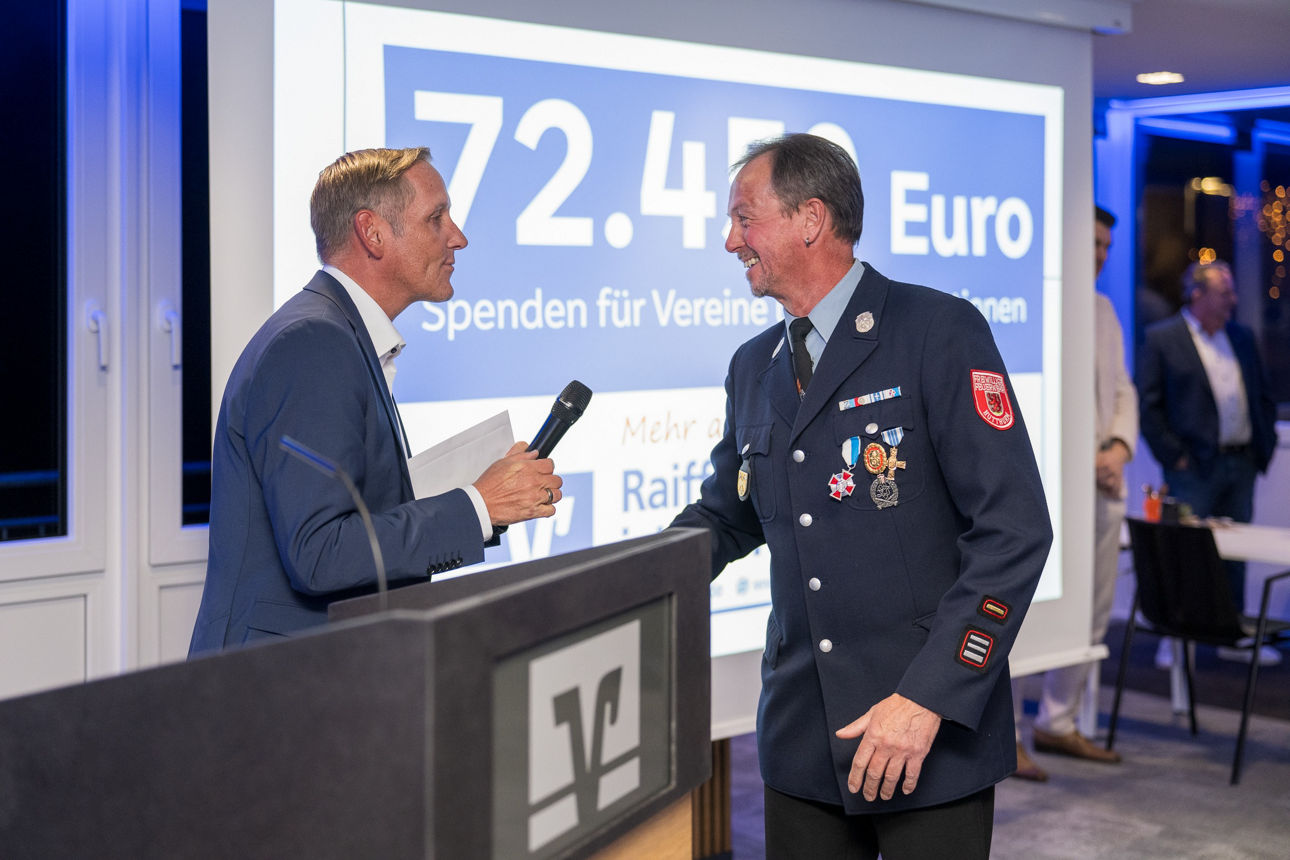 Ein Mann mit einem Mikrofon wärend er einem Mann die Hand reicht.