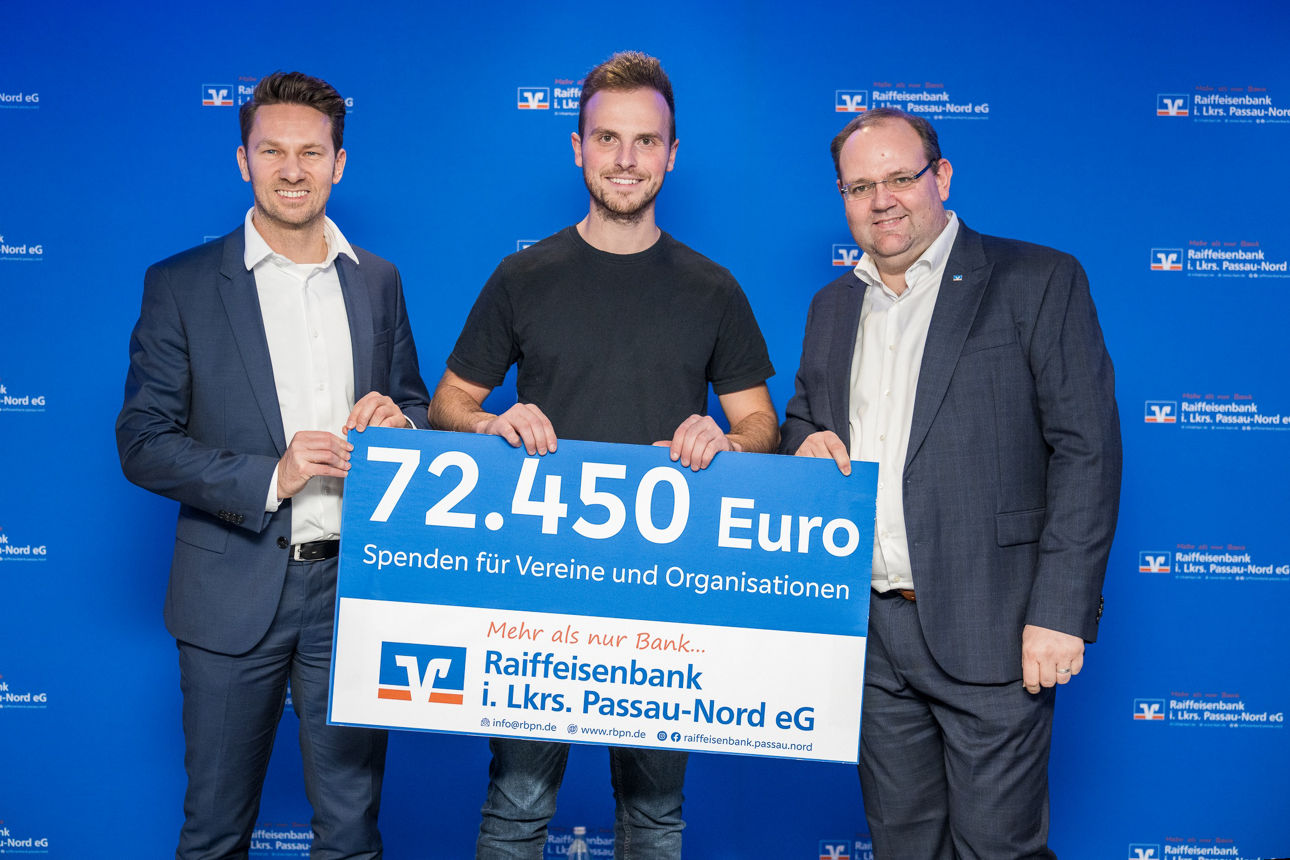 Der Scheck über 72.450 Euro und drei Herren im Hintergrund. 