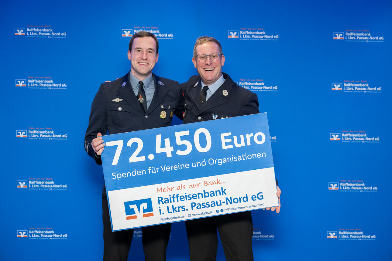 Der Scheck über 72.450 Euro und zwei Herren im Hintergrund. 