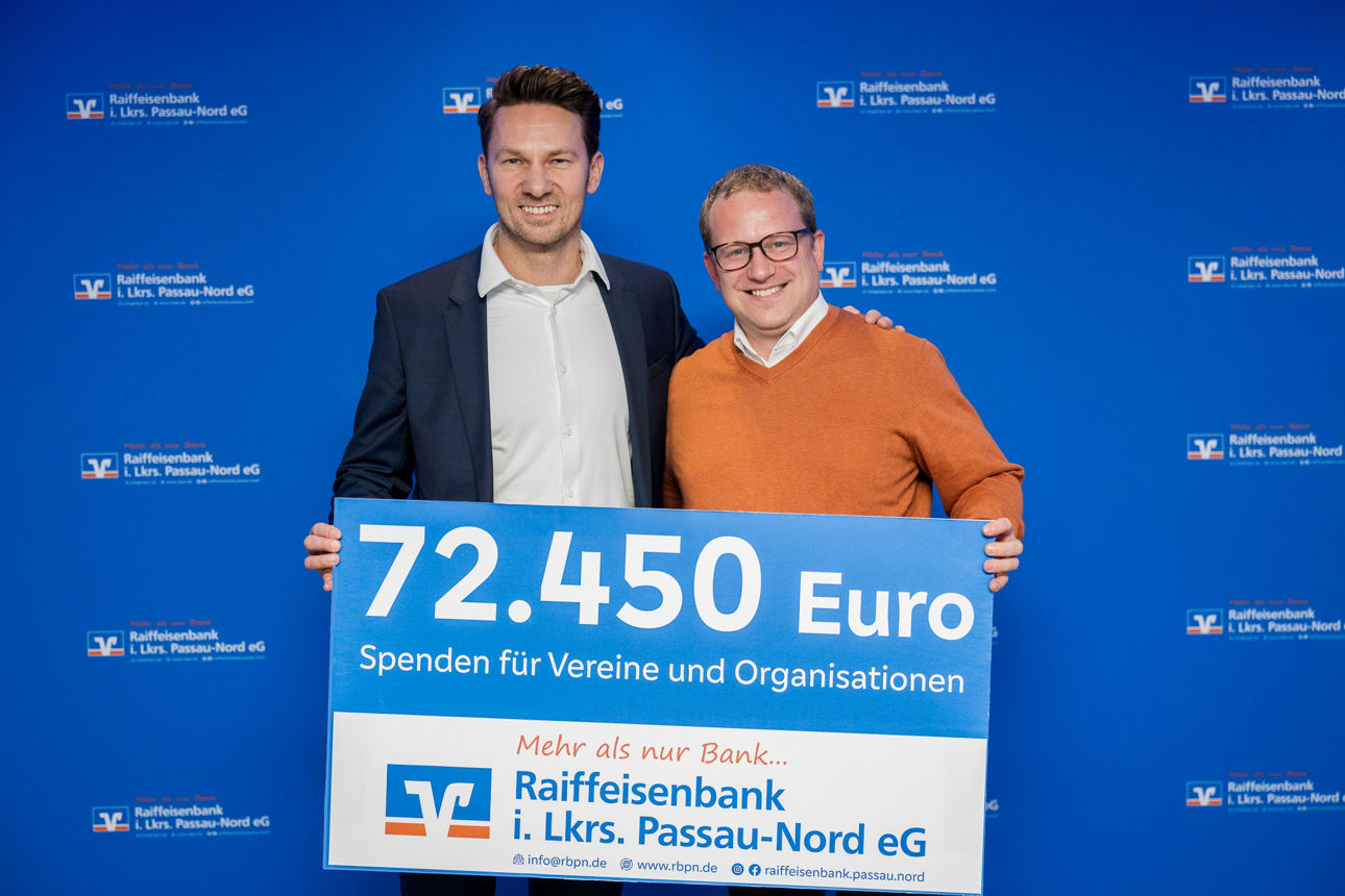 Der Scheck über 72.450 Euro und zwei Herren im Hintergrund. 