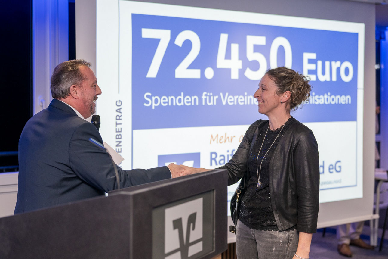 Ein Mann mit einem Mikrofon wärend er einer Frau die Hand reicht.