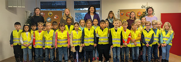 Eine Gruppe von Grundschülern, Lehrern und Mitarbeitern, alle mit leuchtend gelben Sicherheitswesten, posiert für ein Foto.