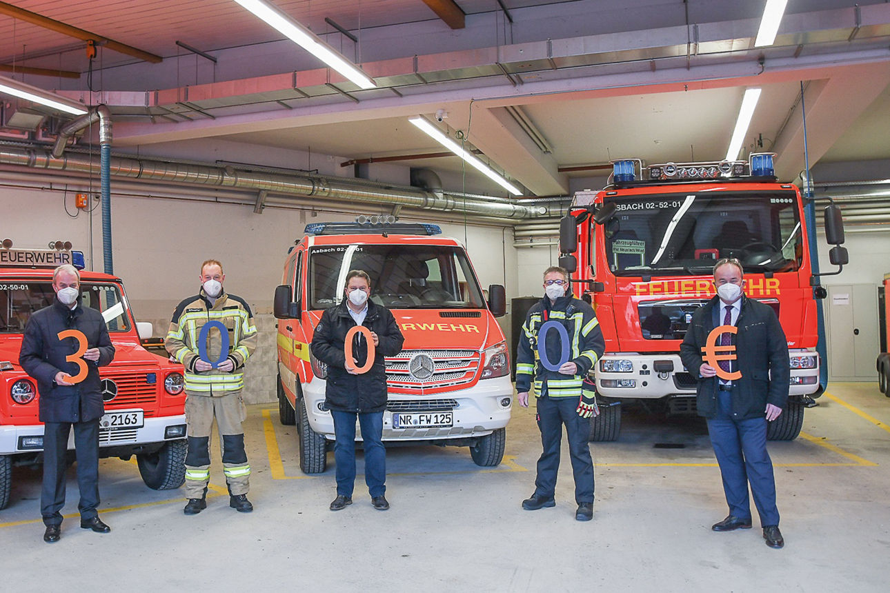Mitglieder der Freiwiligen Feuerwehr Neustadt und der Vorstand der Bank stehen im Gerätehaus vor drei Einsatzfahrzeugen
