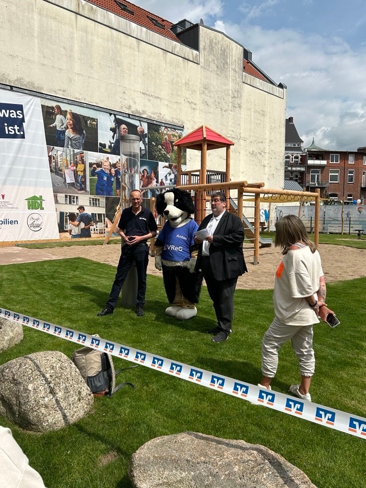 Mehrere Personen und ein Maskottchen stehen vor dem neuen Spielplatz.