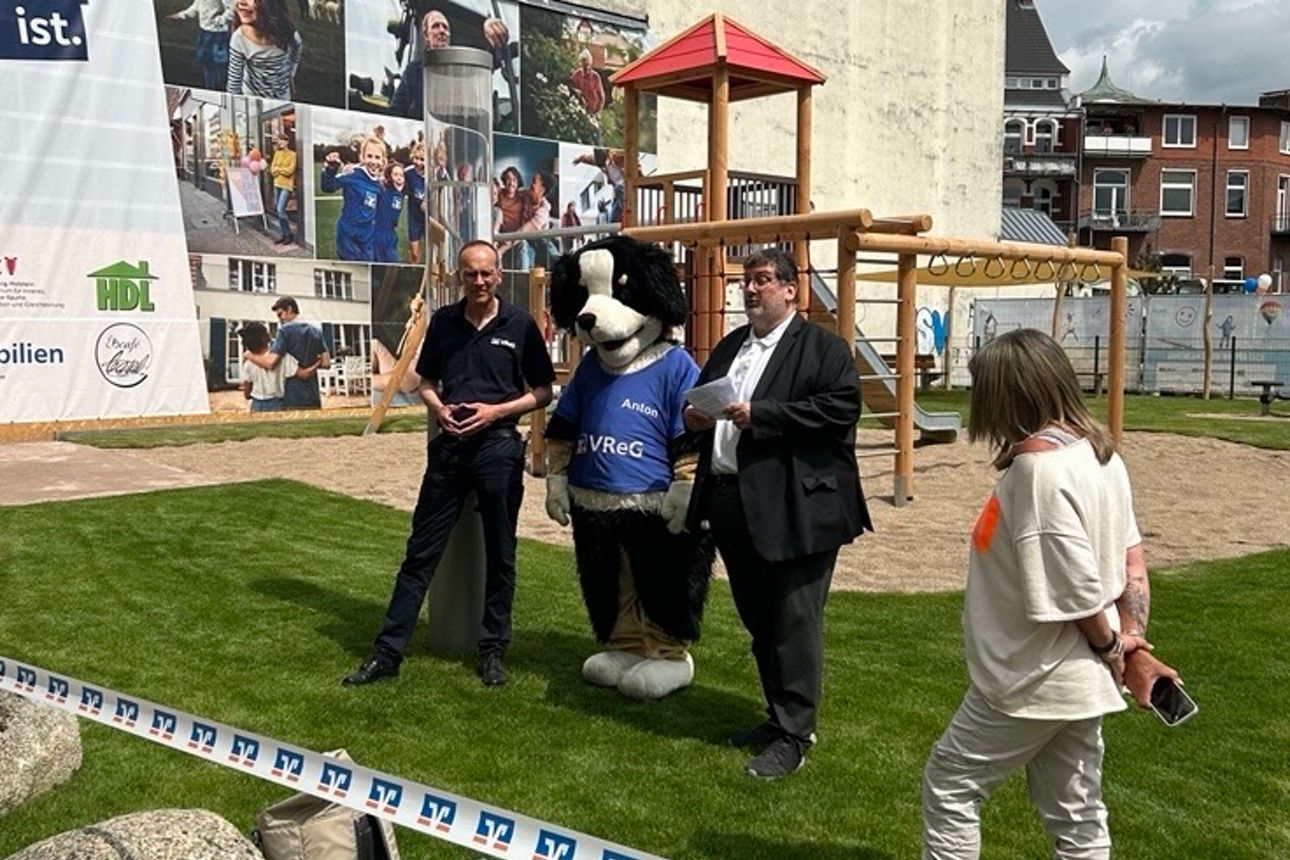 Mehrere Personen und ein Maskottchen stehen vor dem neuen Spielplatz.