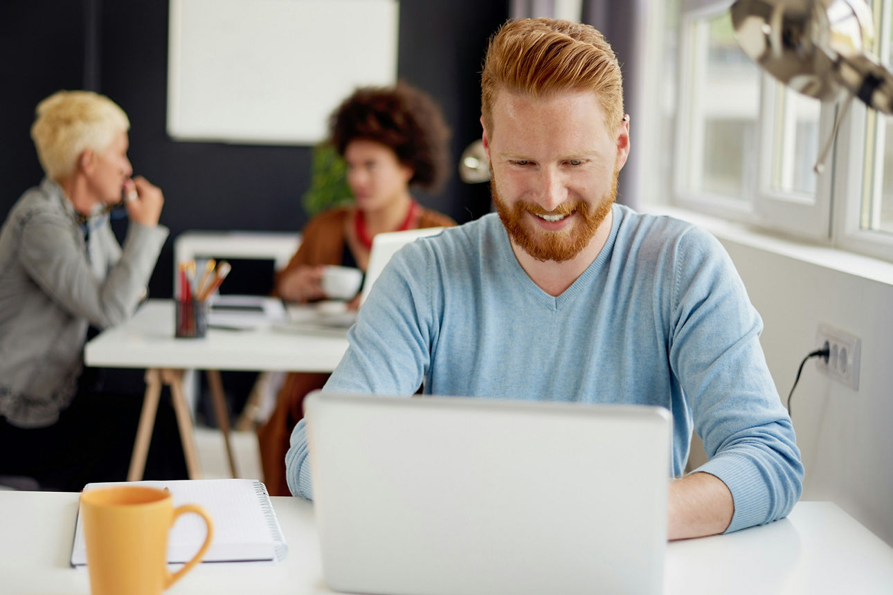 Ein Mann sitzt allein mit Laptop am Tisch, zwei Frauen unterhalten sich im Hintergrund