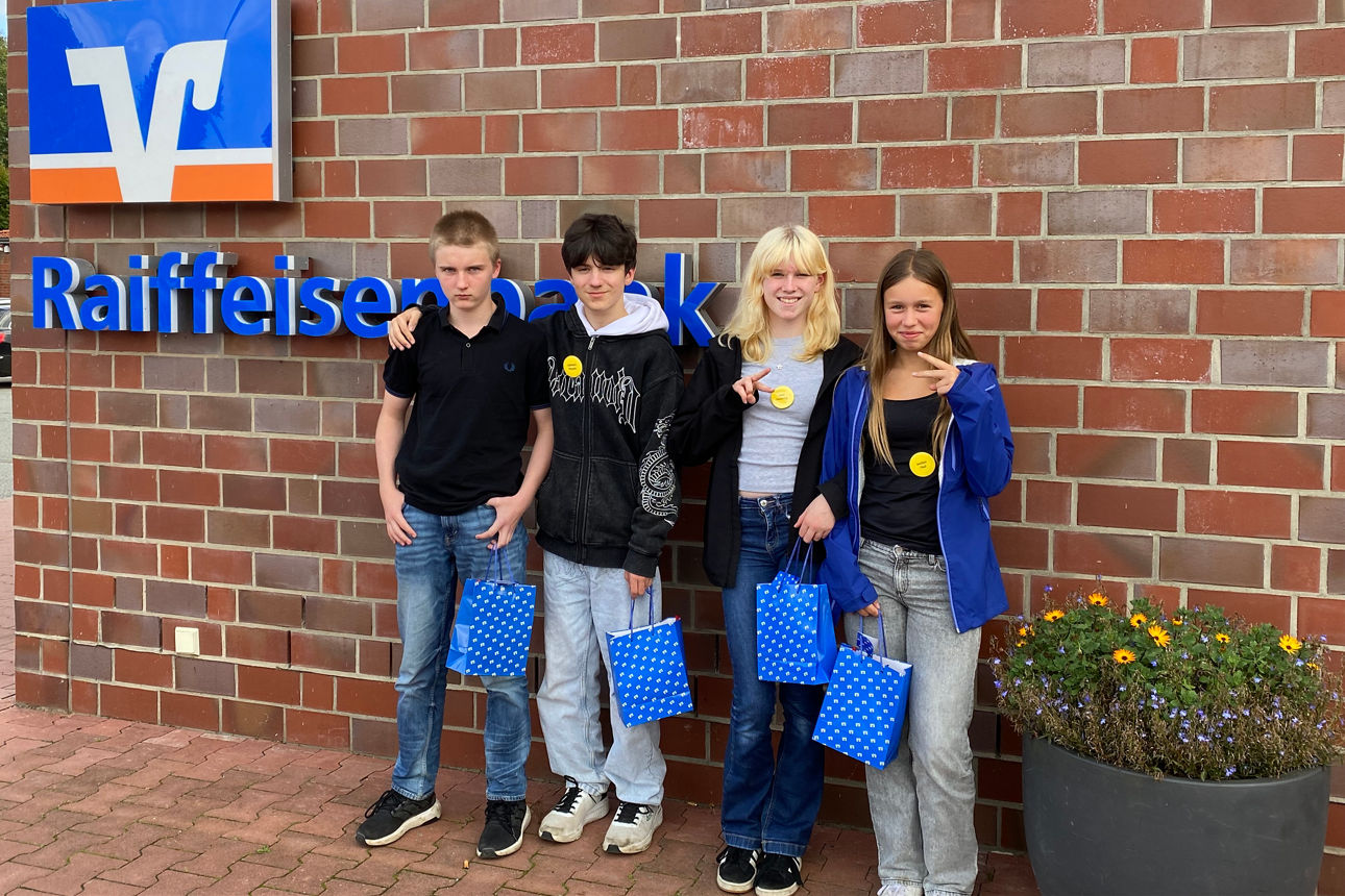 Vier Schüler:innen stehen vor einer Bankfiliale.