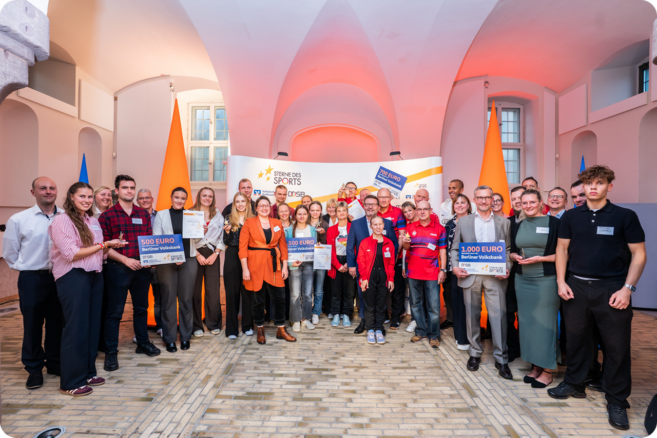 Eine Gruppe von Menschen stehen im Halbkreis und einige halten Gewinnschecks 