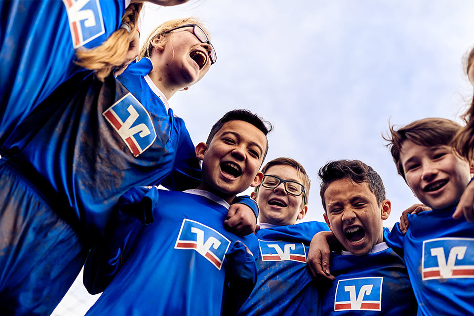 Eine Kinder-Fußballmannschaft in Volksbank-Trikots steht im Kreis und jubelt