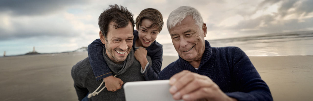 Ein älterer Herr schaut mit seinem Sohn und seinem Enkel auf sein Handy