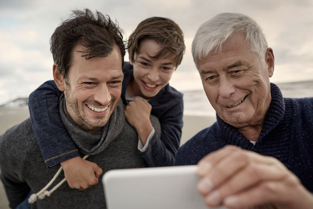Ein älterer Herr schaut mit seinem Sohn und seinem Enkel auf sein Handy