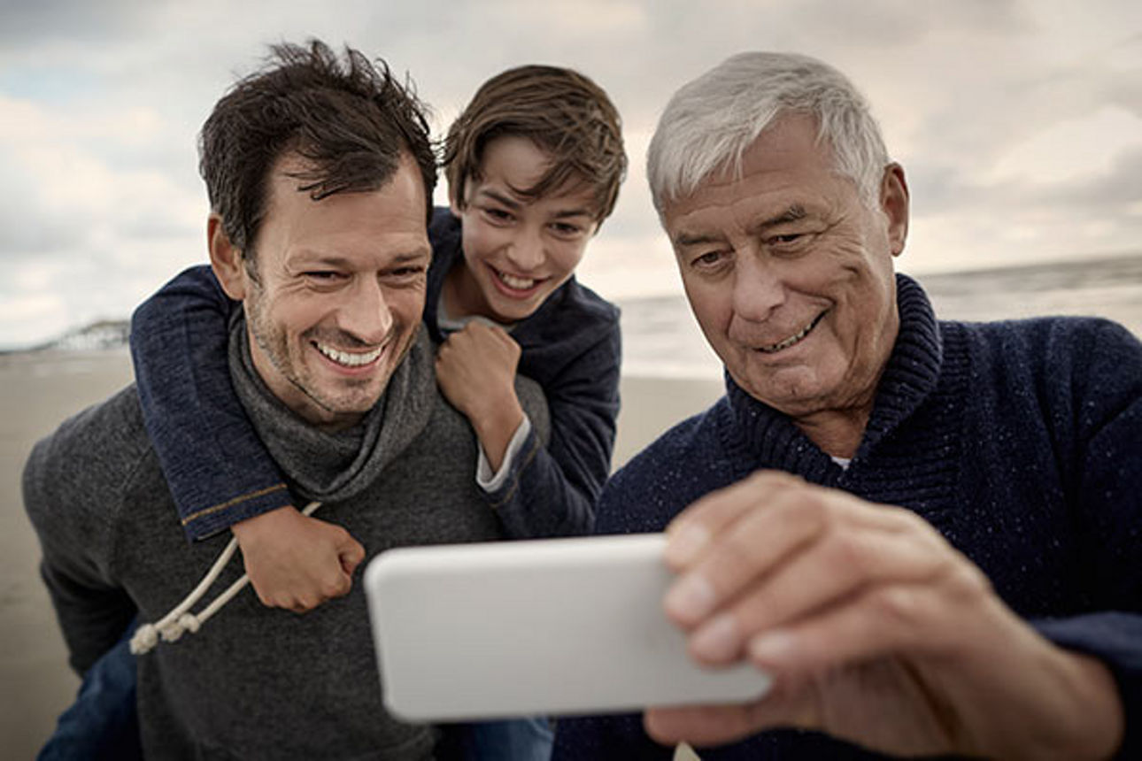 Großvater, Vater und Sohn stehen am Strand und machen ein Selfie