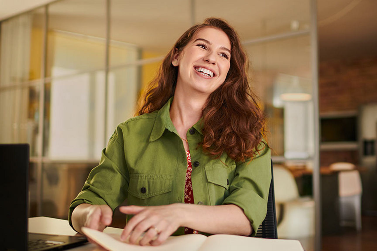 Eine junge Frau sitzt lächelnd am Schreibtisch