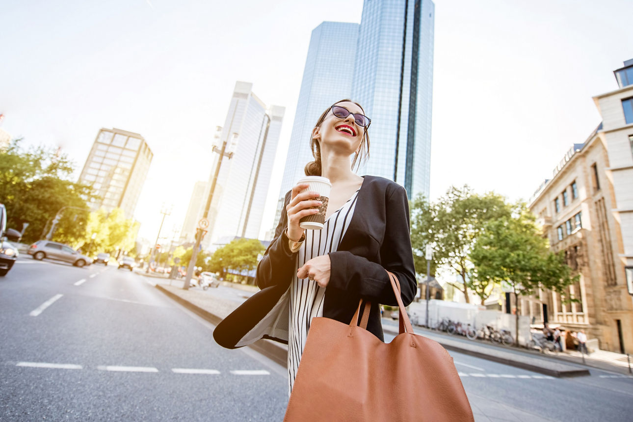 FVB Tagesgeld Junge Dame läuft mit einem Kaffee in der Hand durch die Innenstadt von Frankfurt