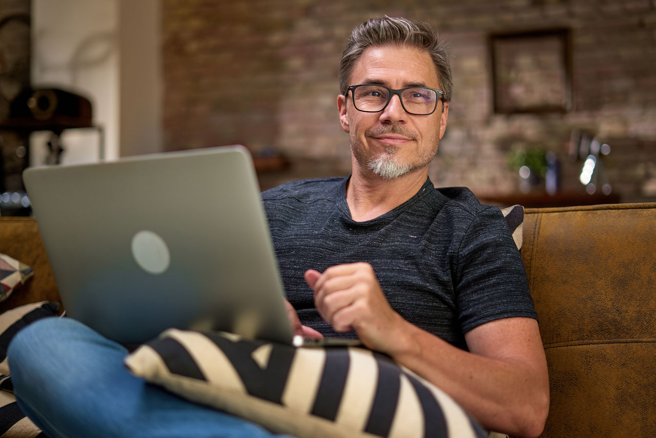 Ein Unternehmer sitzt auf dem Sofa und hat ein Notebook in der Hand