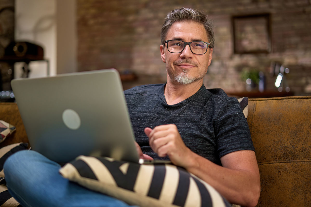 Ein Unternehmer sitzt auf dem Sofa und hat ein Notebook in der Hand