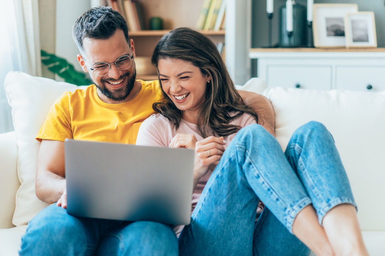 Glückliches Päarchen sitz auf einem Sofa und schaut auf einen Laptop