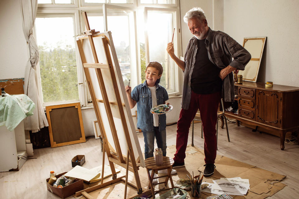 Opa und Enkel stehen mit Pinseln neben einer Leinwand