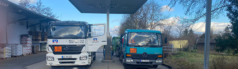 Zwei Lastwagen, ein weißer und ein blaugrüner, sind an einer Tankstelle geparkt und bereit zum Tanken.