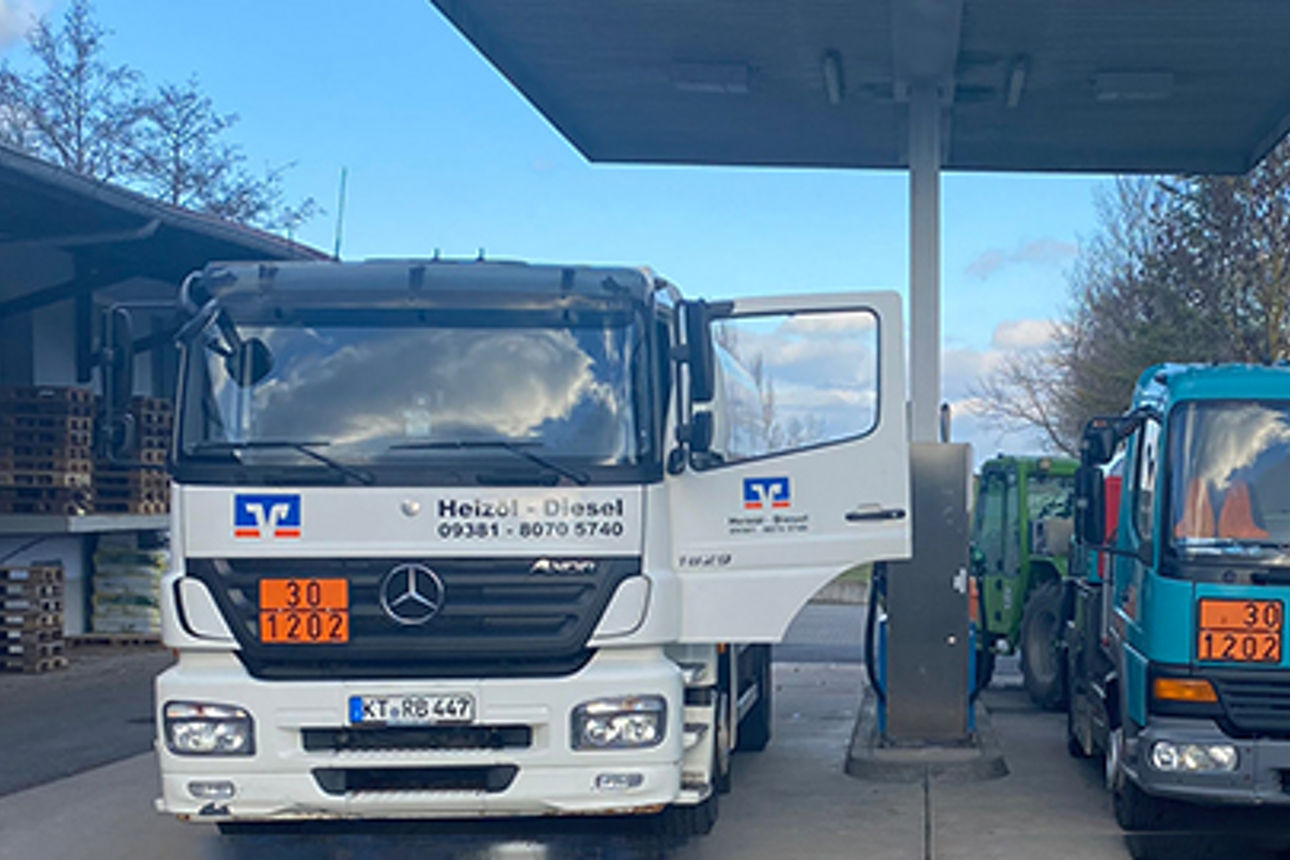 Zwei Lastwagen, ein weißer und ein blaugrüner, sind an einer Tankstelle geparkt und bereit zum Tanken.