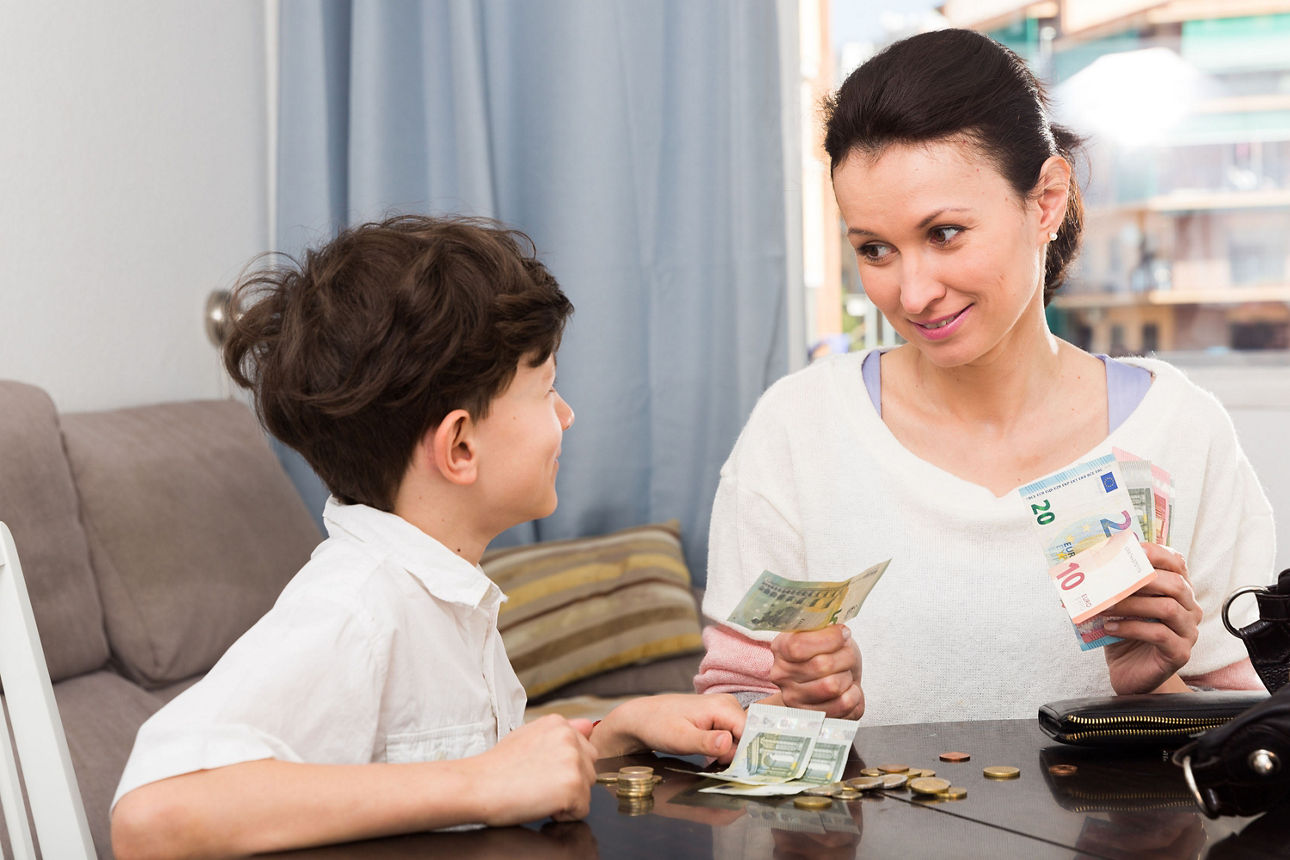 Mutter sitzt mit ihrem Sohn am Tisch und gibt ihm Taschengeld.