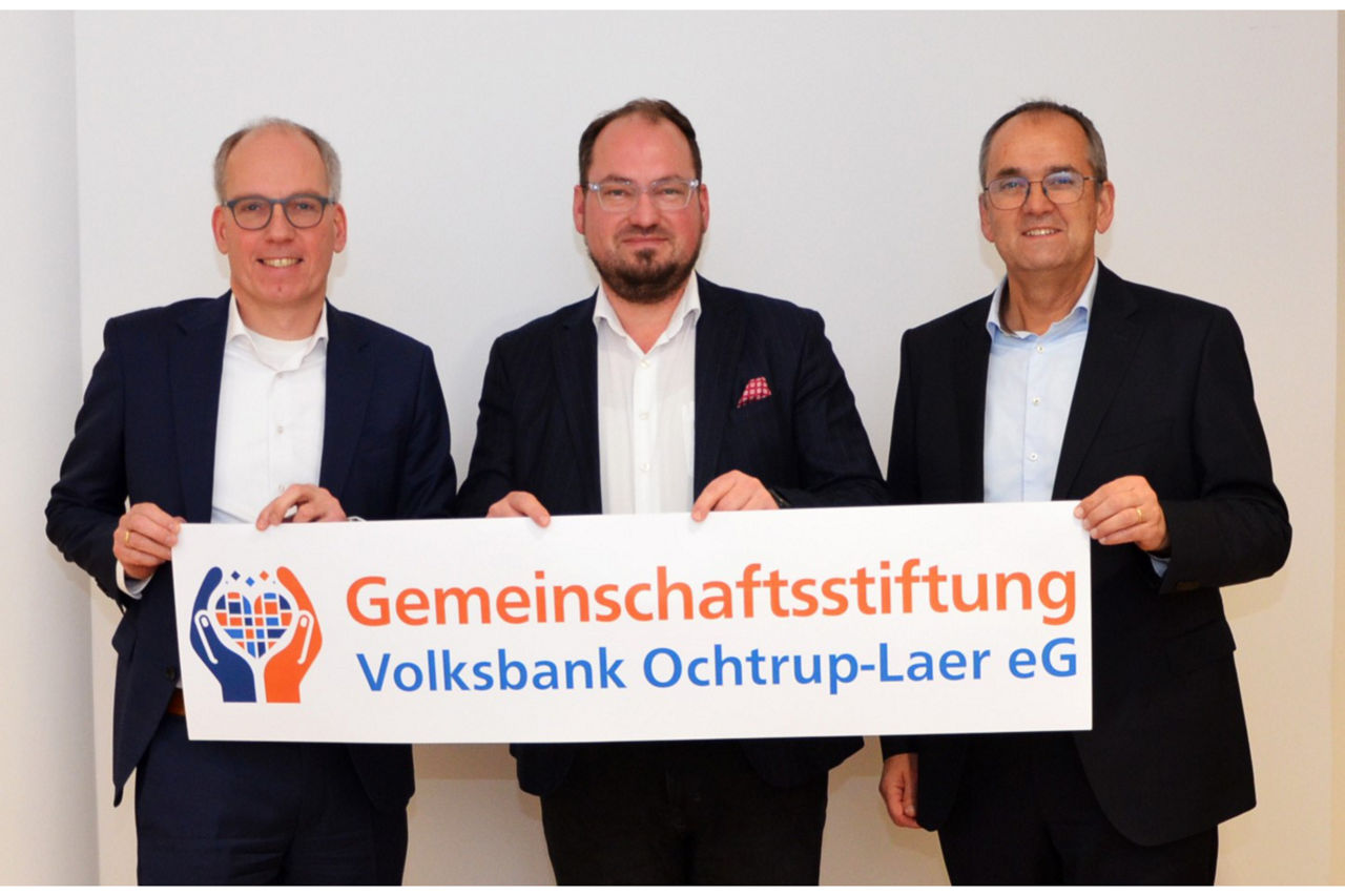 Drei Männer im Anzug halten ein Schild "Gemeinschaftsstiftung Volksbank Ochtrup-Laer eG"