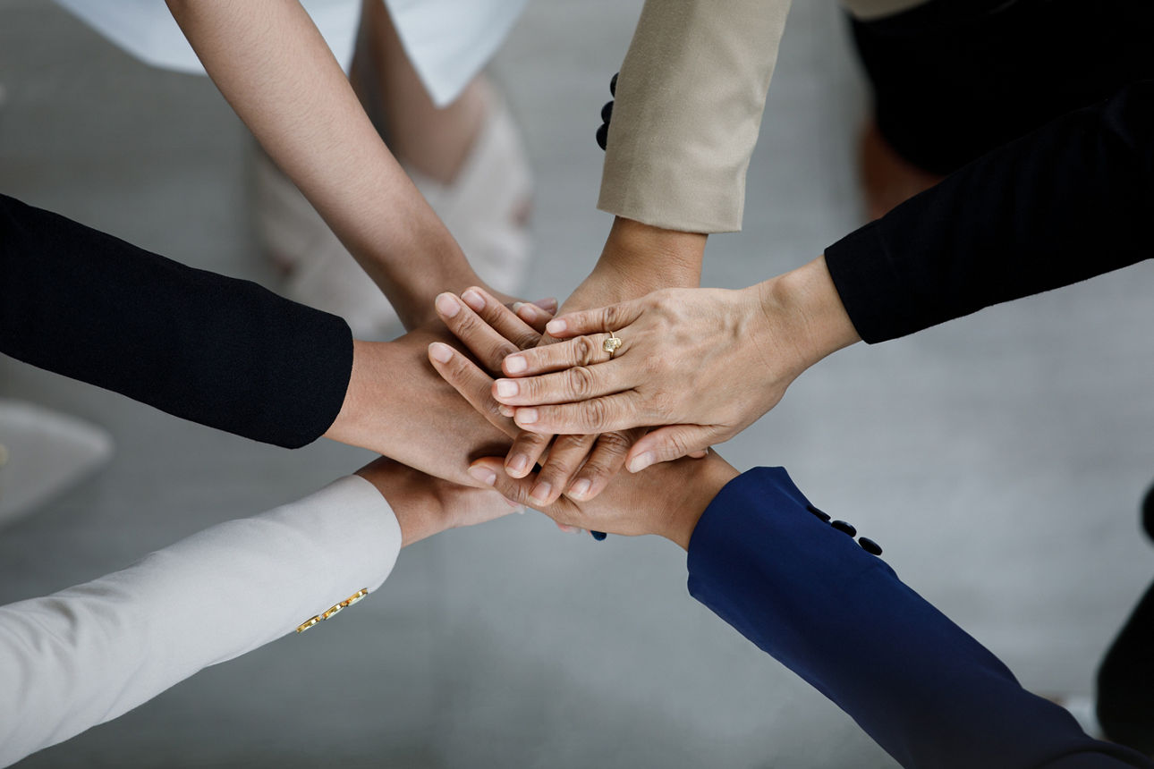 Mehrere Hände in einem Kreis, übereinandergelegt, symbolisieren Teamwork und Zusammenhalt.