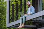 Mann sitzt mit Laptop auf dem Vorsprung eines Hauses