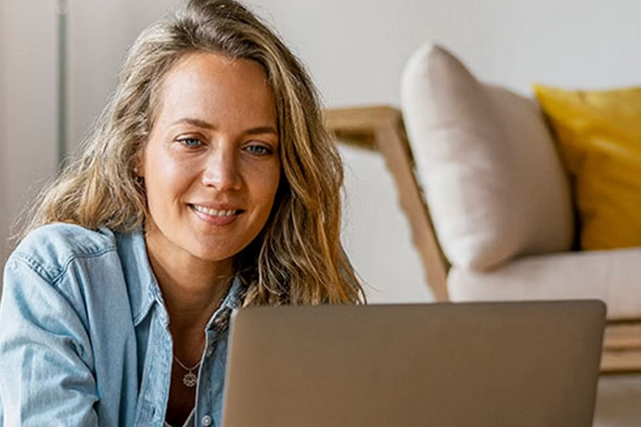 Junge Frau schaut lächelnd auf ihren Laptopbildschirm