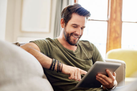 Shot of a happy young man using a digital tablet on the sofa at home
