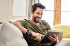 Lächelnder Mann sitzt auf dem Sofa mit einem Tablet in der Hand 