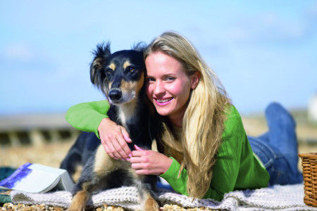 Frau strahlt in die Kamera und umarmt ihren Hund