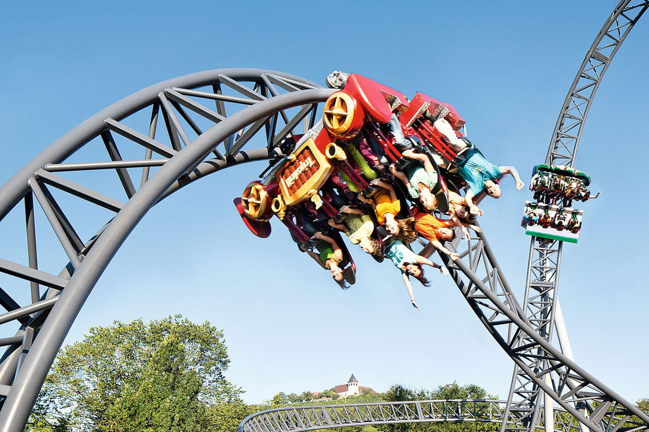 Achterbahn mit Fahrgästen in rasanter Kurve eines Freizeitparks.