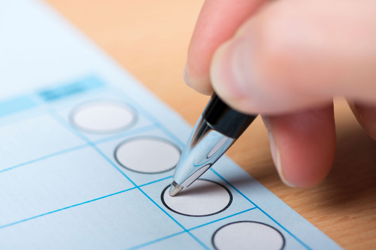 Hand steckt ein Blatt in eine weiße Wahlbox