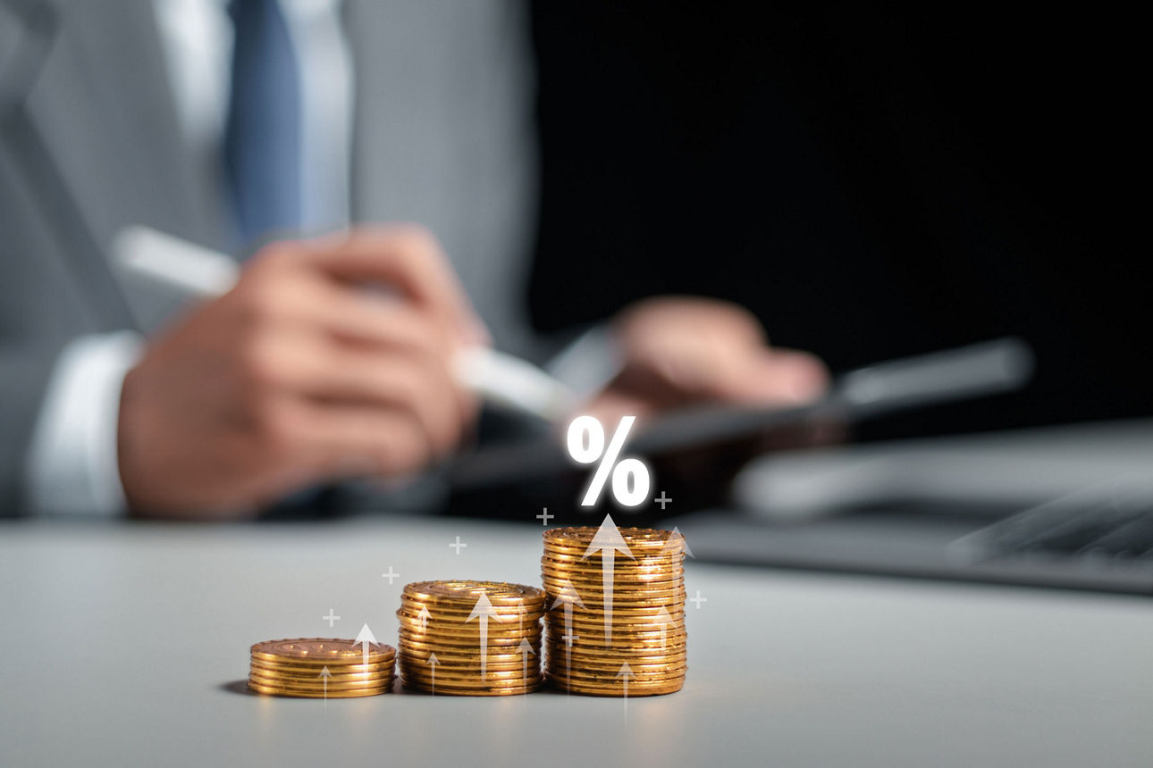 Gestapelte Münzen mit Prozentzeichen und Pfeil nach oben als Symbol für Wachstum und Zinsen.