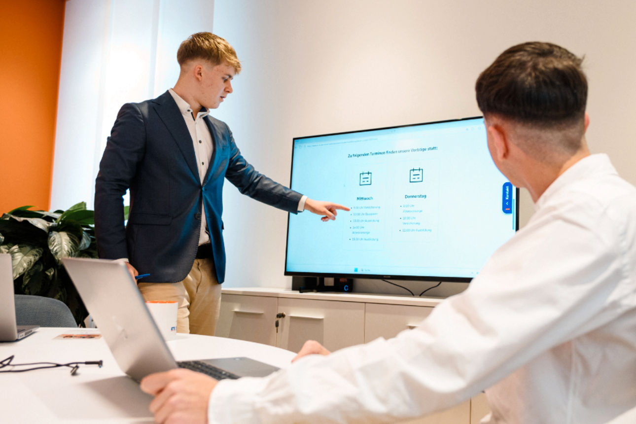 Junger Banker präsentiert Kollegen etwas am Bildschirm