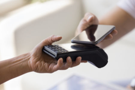 Eine Hand hält ein Kartenlesegerät eine andere Hand hält ein Smartphone dagegen