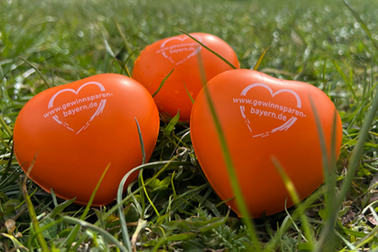 Drei orange Schaumstoffherzen liegen in einer grünen Wiese und der Logoaufdruck "Gewinnsparverein" ist zu lesen.