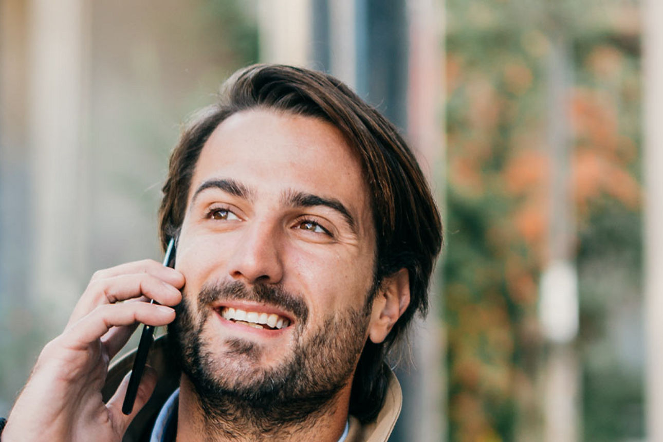 Mann telefoniert und lächelt mit Blick nach oben.