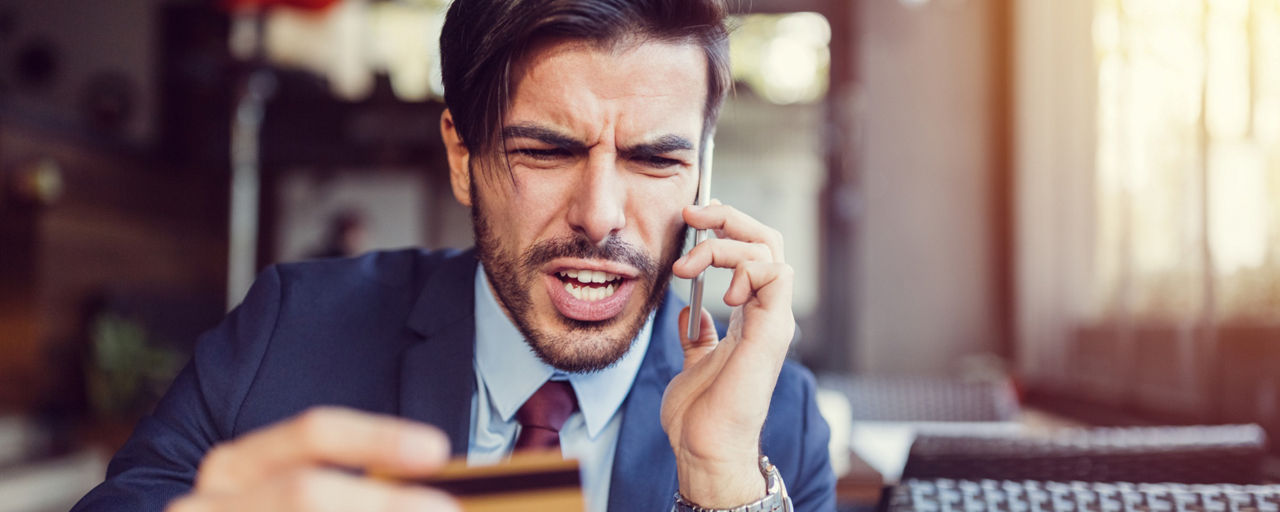 Augeregter Mann am Telefon hält seine Kreditkarte in der Hand