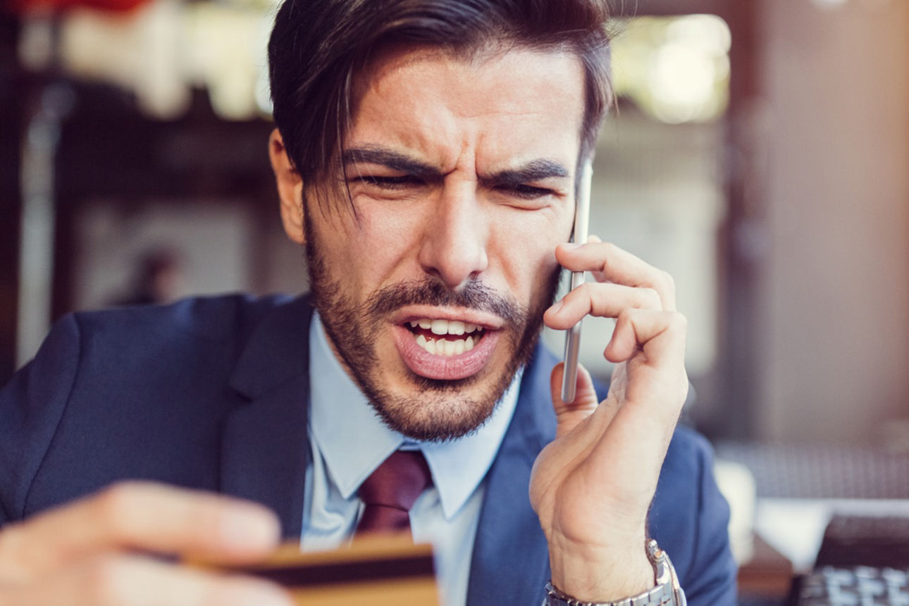 Augeregter Mann am Telefon hält seine Kreditkarte in der Hand