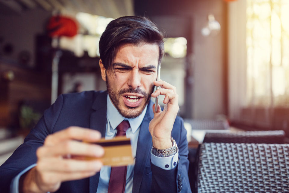 Augeregter Mann am Telefon hält seine Kreditkarte in der Hand