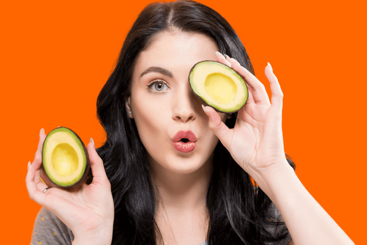 Person hält zwei Avocadohälften vor orangefarbenem Hintergrund, eine in jeder Hand.