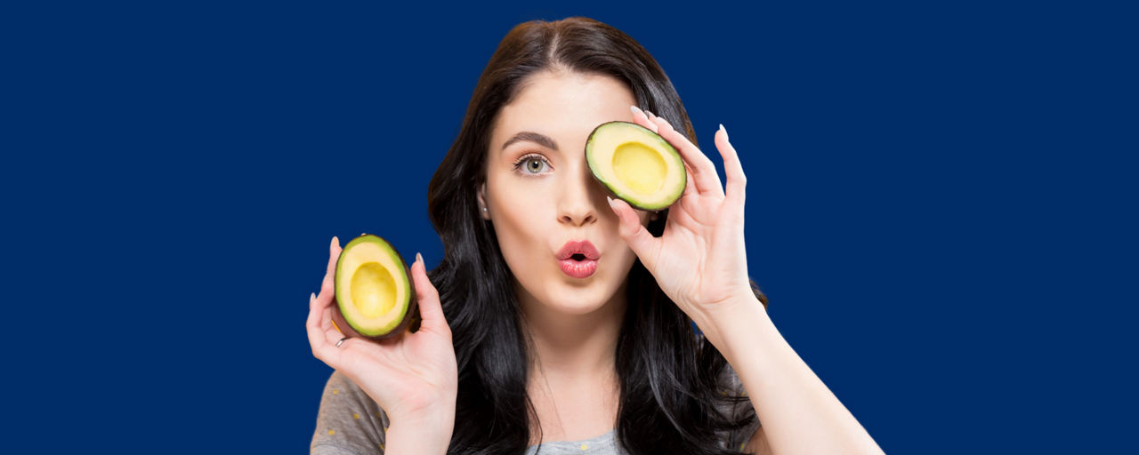 Frau mit einer halbierten Avocado vor dem Auge und eine in der Hand