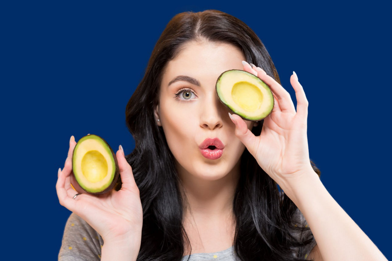 Frau mit einer halbierten Avocado vor dem Auge und eine in der Hand.