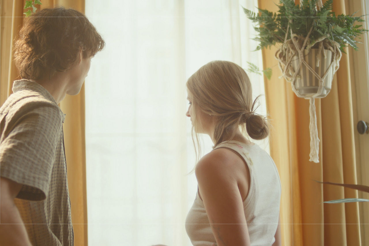 Ein Mann und eine Frau stehen mit dem Blick zum Fenster in einer hell erleuchteten Wohnung. Ein Mann und eine Frau stehen mit dem Blick zum Fenster in einer hell erleuchteten Wohnung.