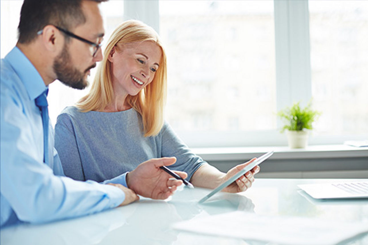 Ein Mann in Hemd und Krawatte sitzt am Tisch mit einer Frau und erklährt ihr auf dem Ipad