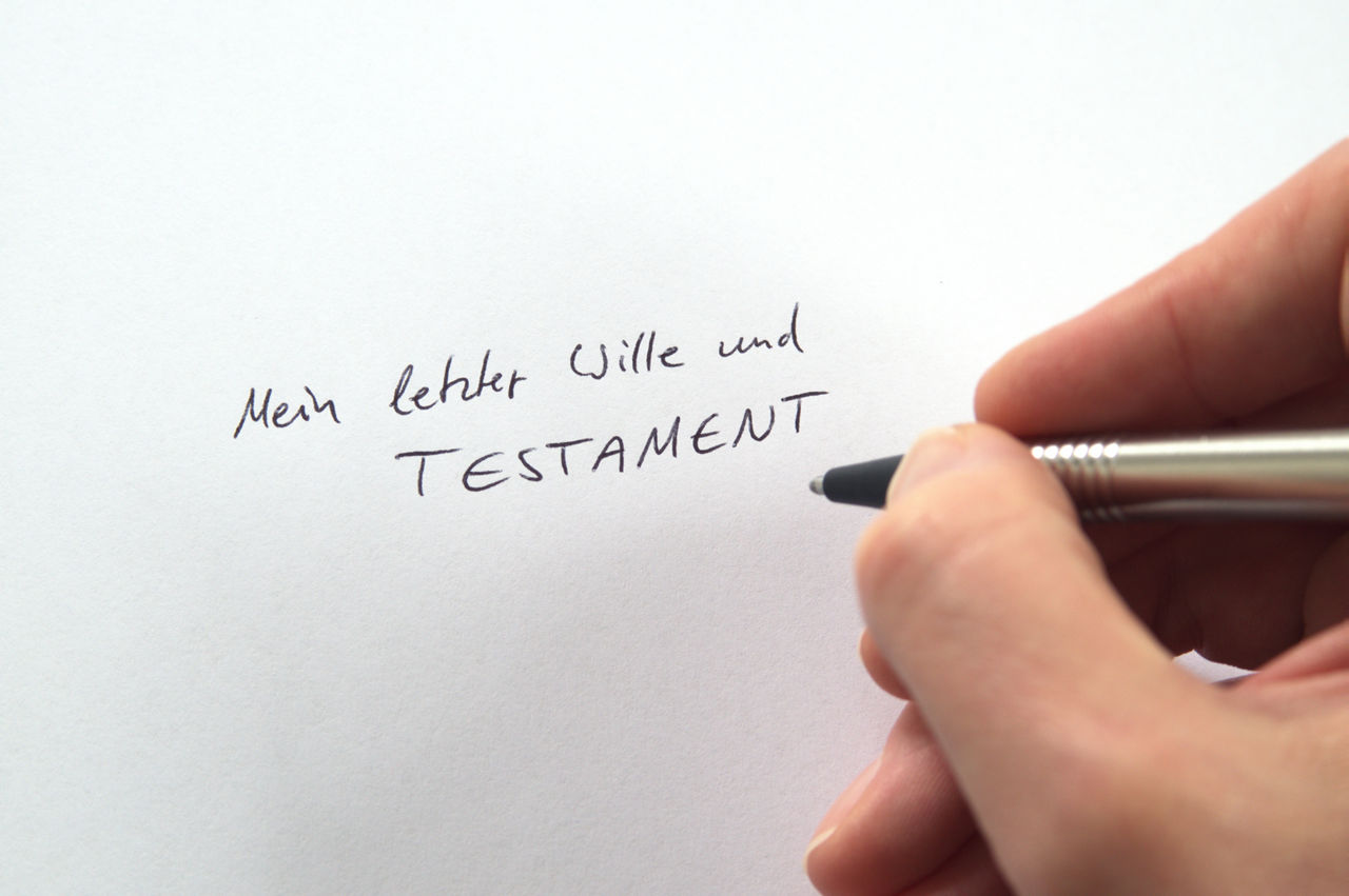 Hand mit Stift im Vordergrund schreibt etwas auf ein Blatt Papier