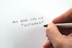 Hand schreibt „Mein letzter Wille und Testament“ auf ein Blatt Papier